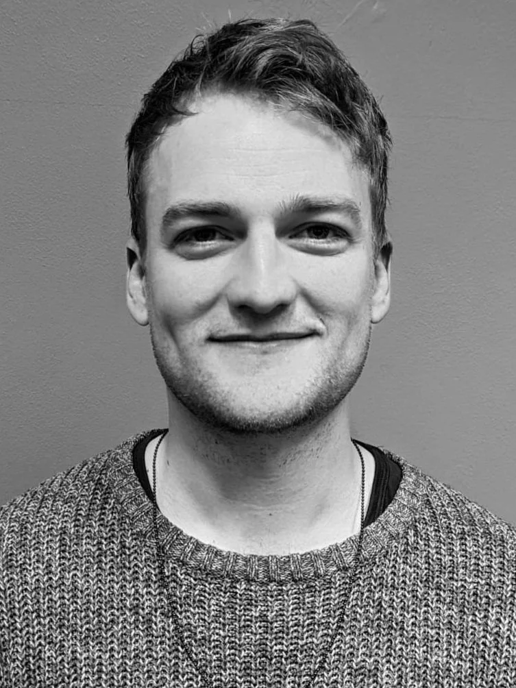 Black and white headshot of Jordan Larkin smiling, wearing a jumper and necklace.