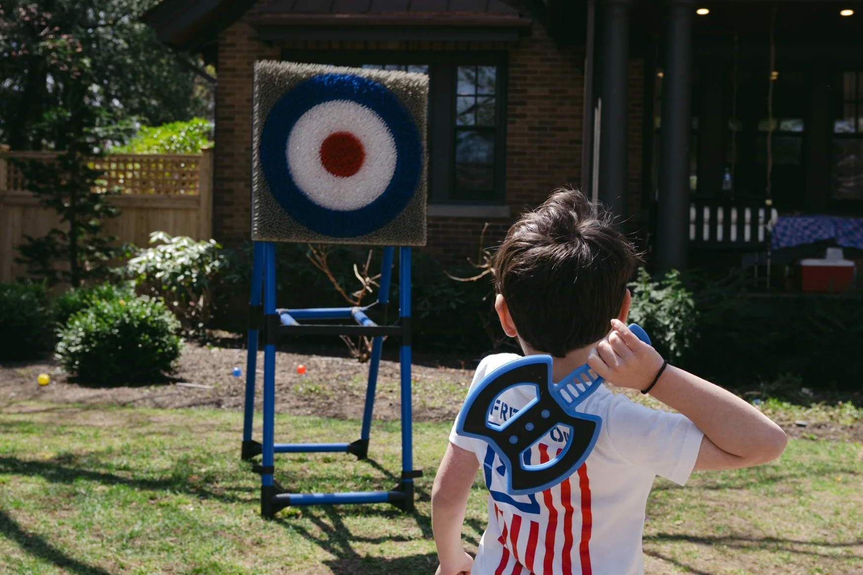 A young boy with a toy axe on his back about to throw an axe at a target in the backyard.