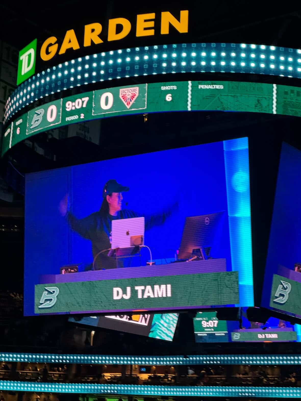 Large digital scoreboard displaying game stats, with a DJ named Tami performing on stage below.