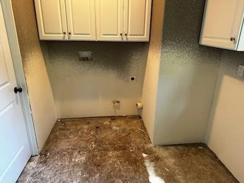 Empty kitchen corner with white cabinets, open space, and a damaged floor.