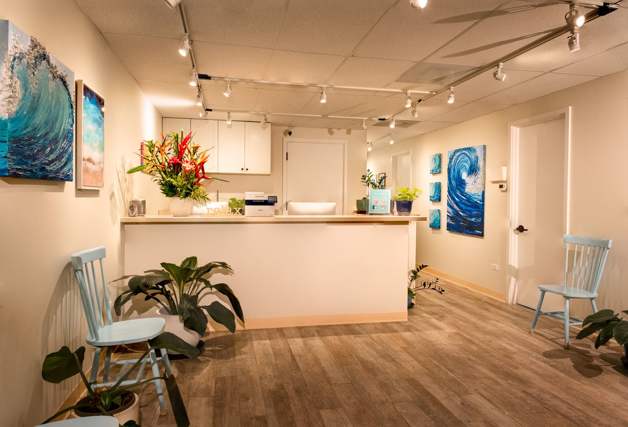 Reception area at Ayurveda Wellness Hawaiʻi in Kailua, with blue seating, fresh flowers, and ocean artwork.