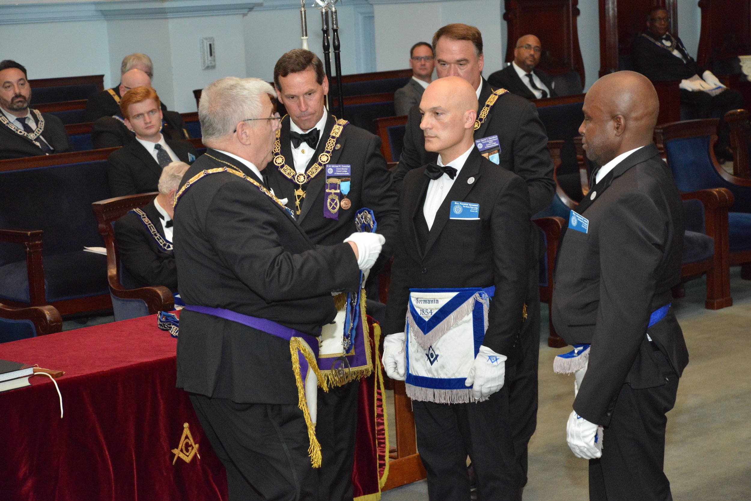  The Senior Grand Deacon, Wor. Ronald Higgins,  investing the Senior Deacon, Bro. Farshid Varasteh, and Junior Deacon, Bro. Jacques Jean, with the jewels and staves of their office 