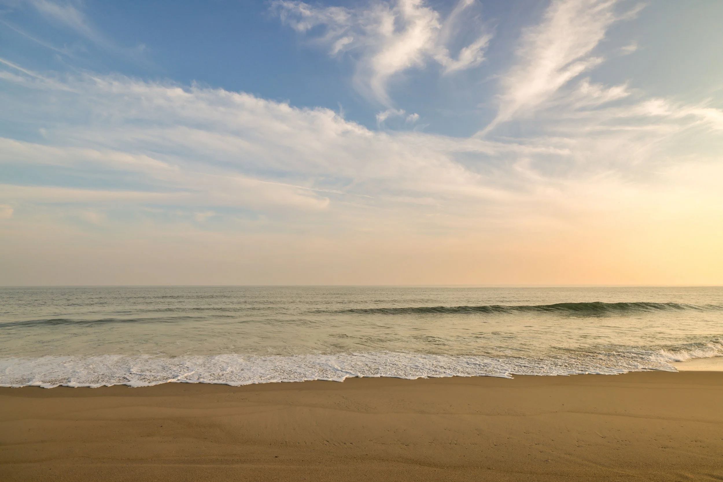 Sunset over the ocean with calm waves gently lapping the sandy beach.