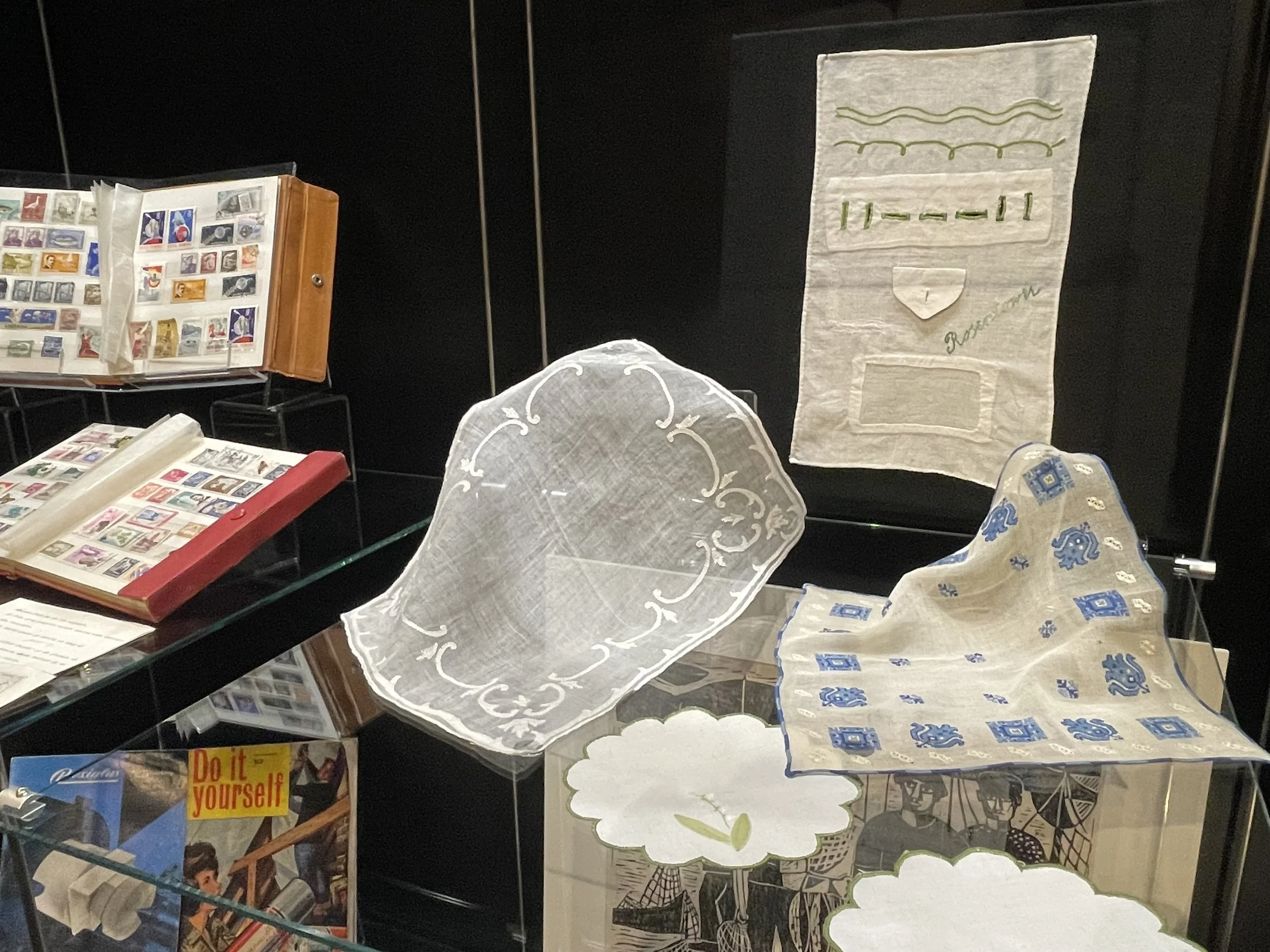 Curiosity cabinet with embroideries stitched by Shula Ullmann as a young child in Romania