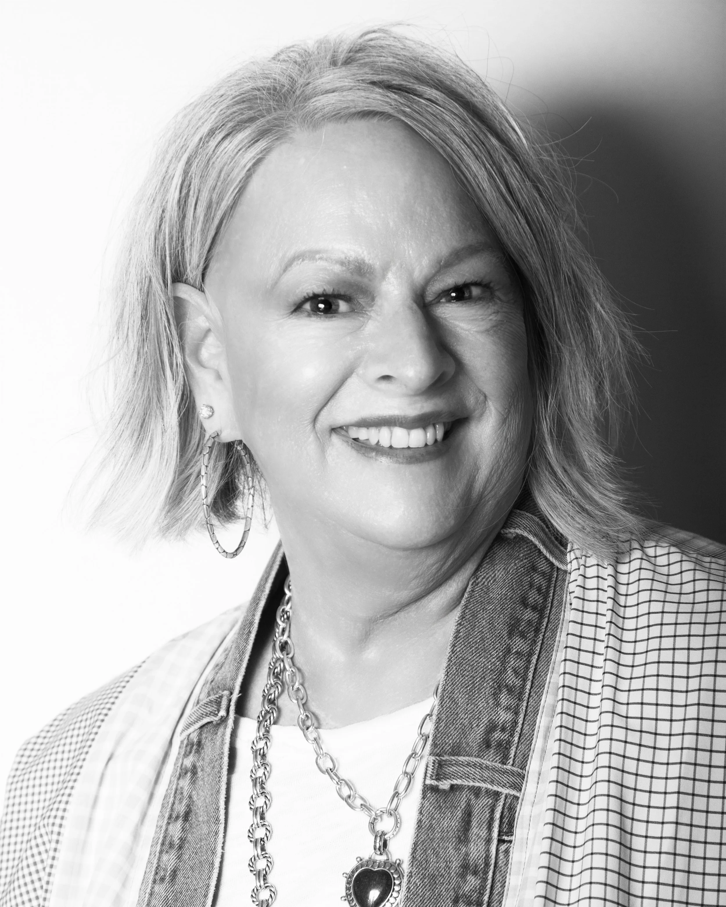Black and white portrait of a smiling woman with short blonde hair wearing a white shirt and dark jacket.