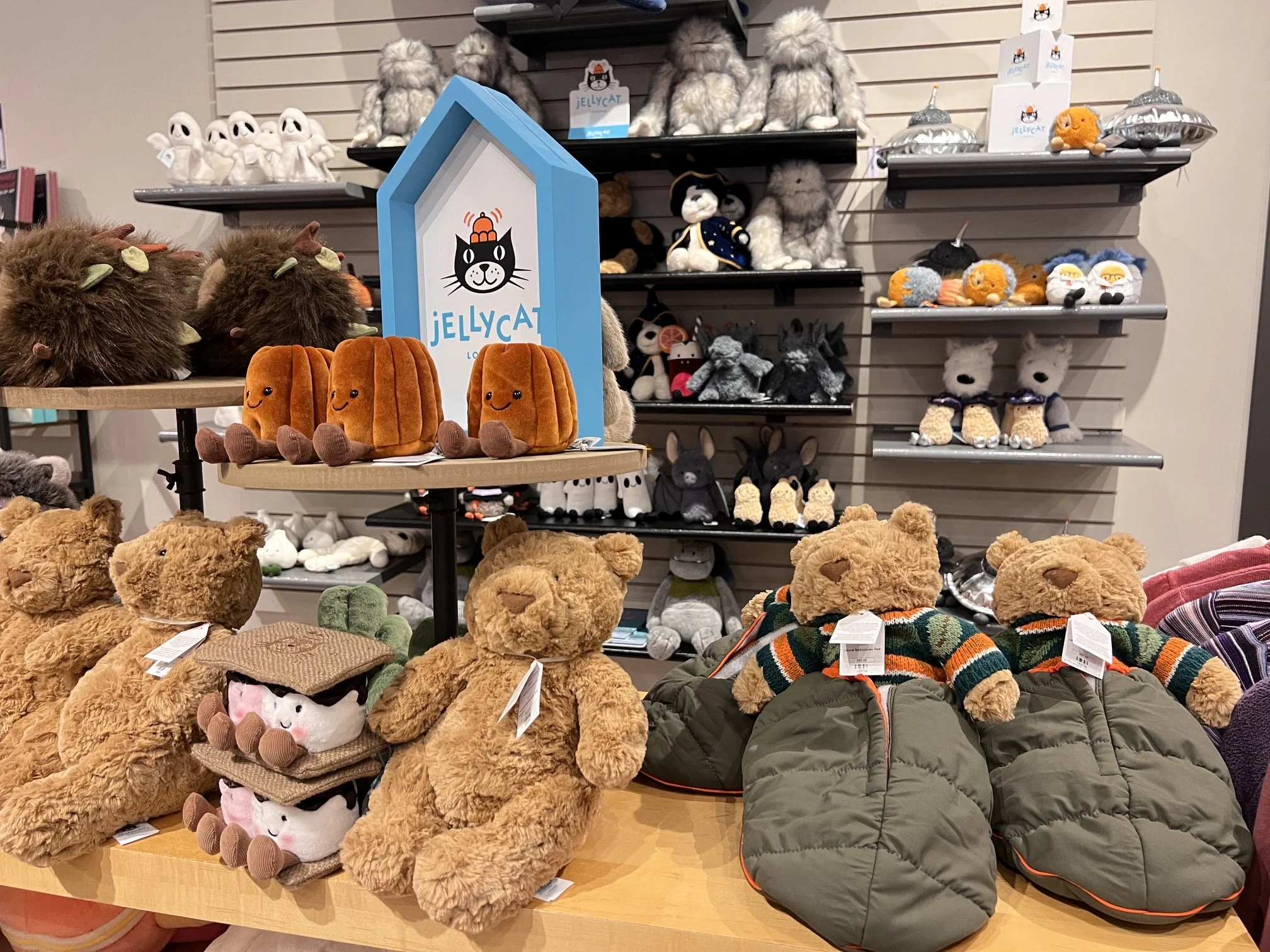Store display with various stuffed animals and boxed toys on wooden shelves, featuring plush lions, pandas, ducks, and elephants, along with boxed toy sets like xylophones and building blocks.