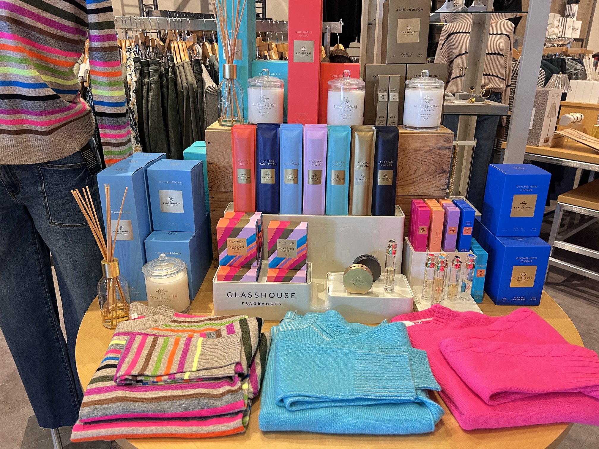 Retail store display with folded clothing, denim jeans, decorative handbags, hats, and accessories on wooden shelves.