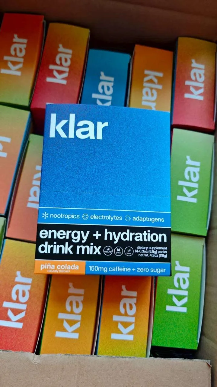 Klar energy and hydration drink mix boxes in assorted flavors with one box close-up. The front box is pineapple flavored with 150mg caffeine and zero sugar.