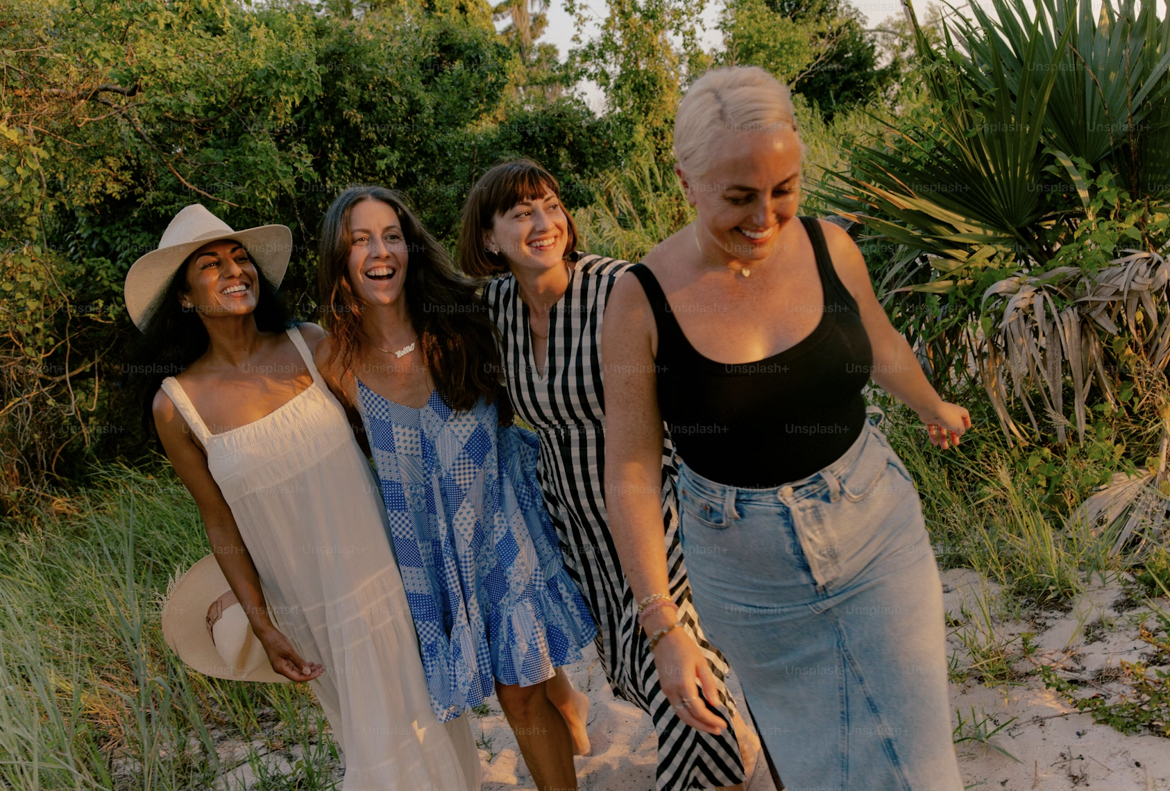 Four women walking outdoors in a natural setting at sunset, smiling and enjoying each other's company.