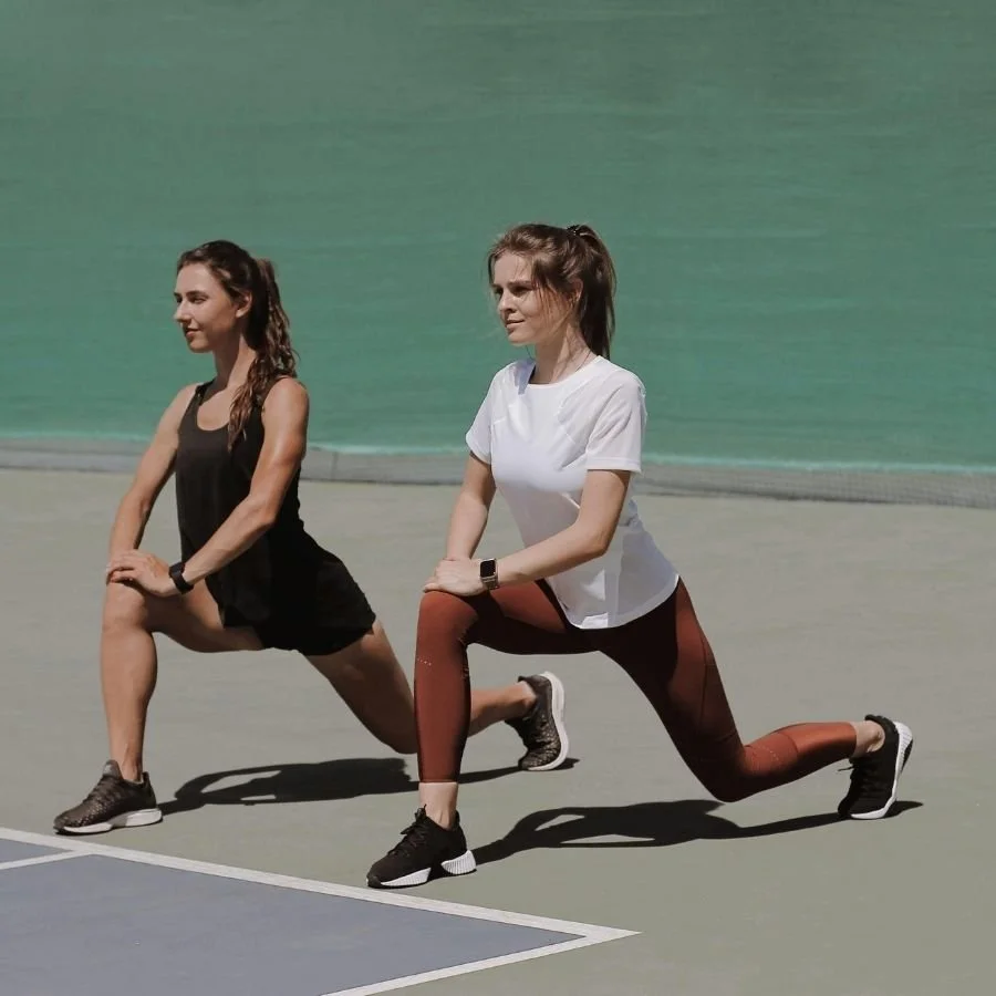 Two women doing walking lunges as part of warm-up routine.