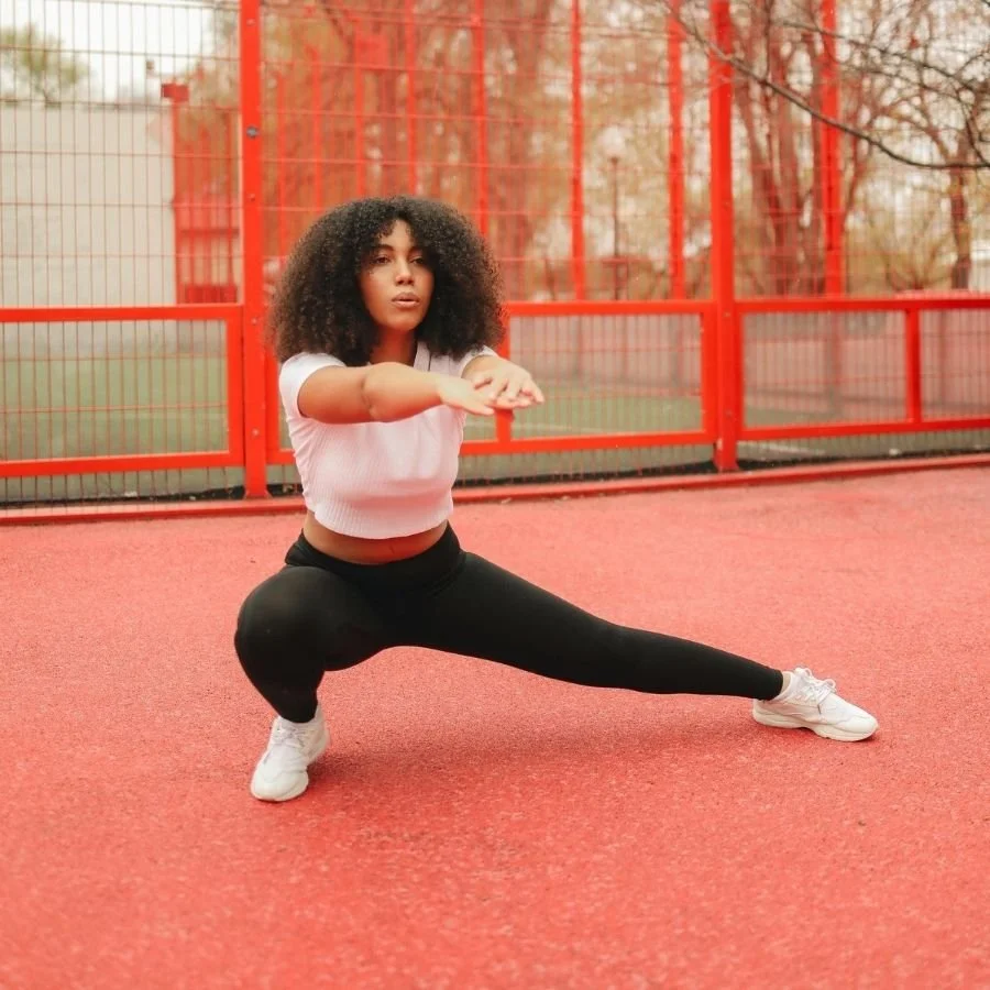Woman performing lateral lunge stretch on outdoor court.