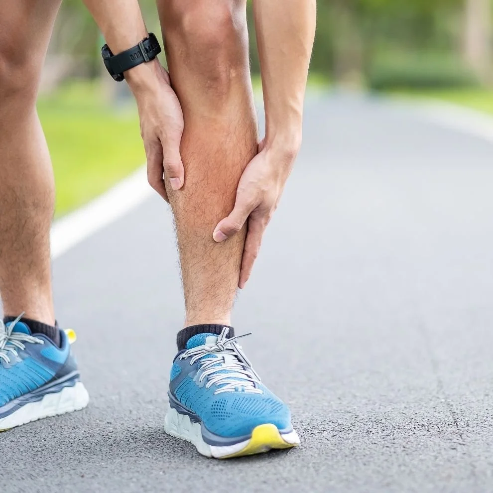 Runner gripping lower leg while experiencing shin splint pain during outdoor training.