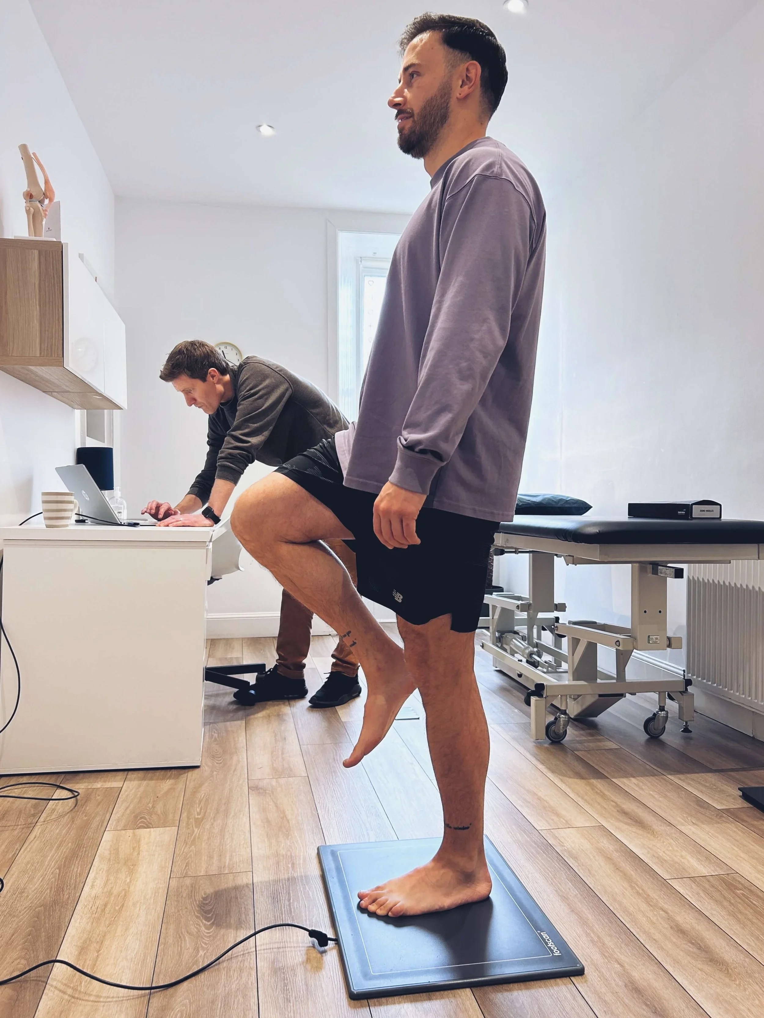 Patient undergoing a foot scan and balance assessment at a physical therapy clinic.