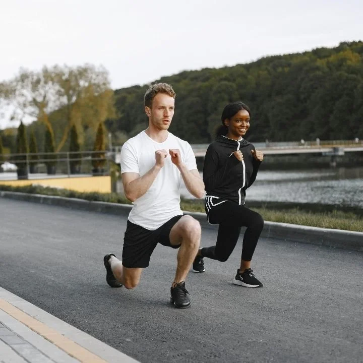 Two runners performing walking lunges during outdoor warm-up.
