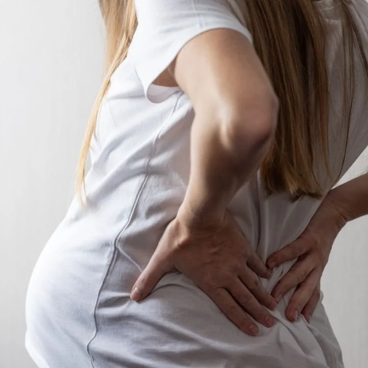 Pregnant woman standing with hands on lower back indicating back discomfort.