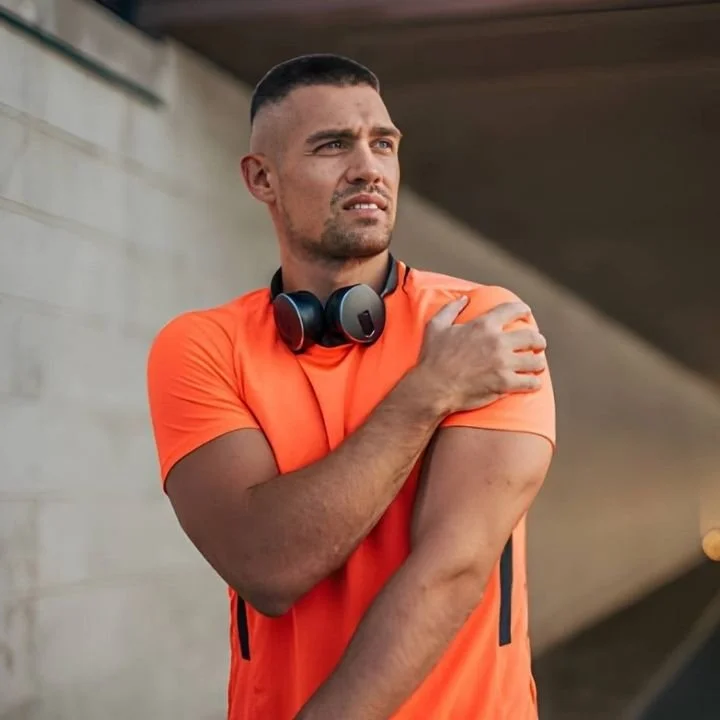 Athletic man holding shoulder in discomfort, showing rotator cuff strain symptoms.