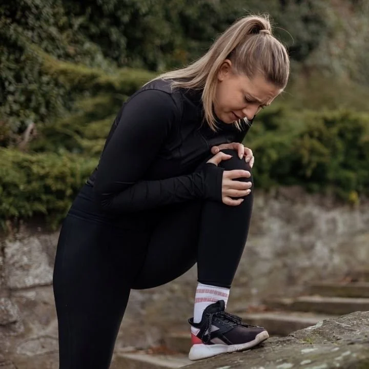 Woman exercising outdoors holding knee after sudden pain.