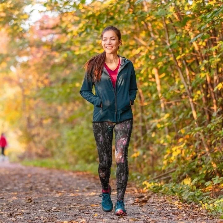 Woman walking on a wooded trail wearing athletic clothing.