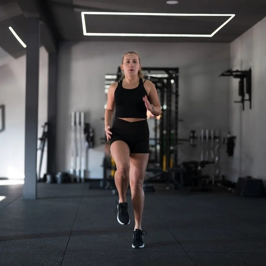 Female athlete doing high knees exercise inside gym.