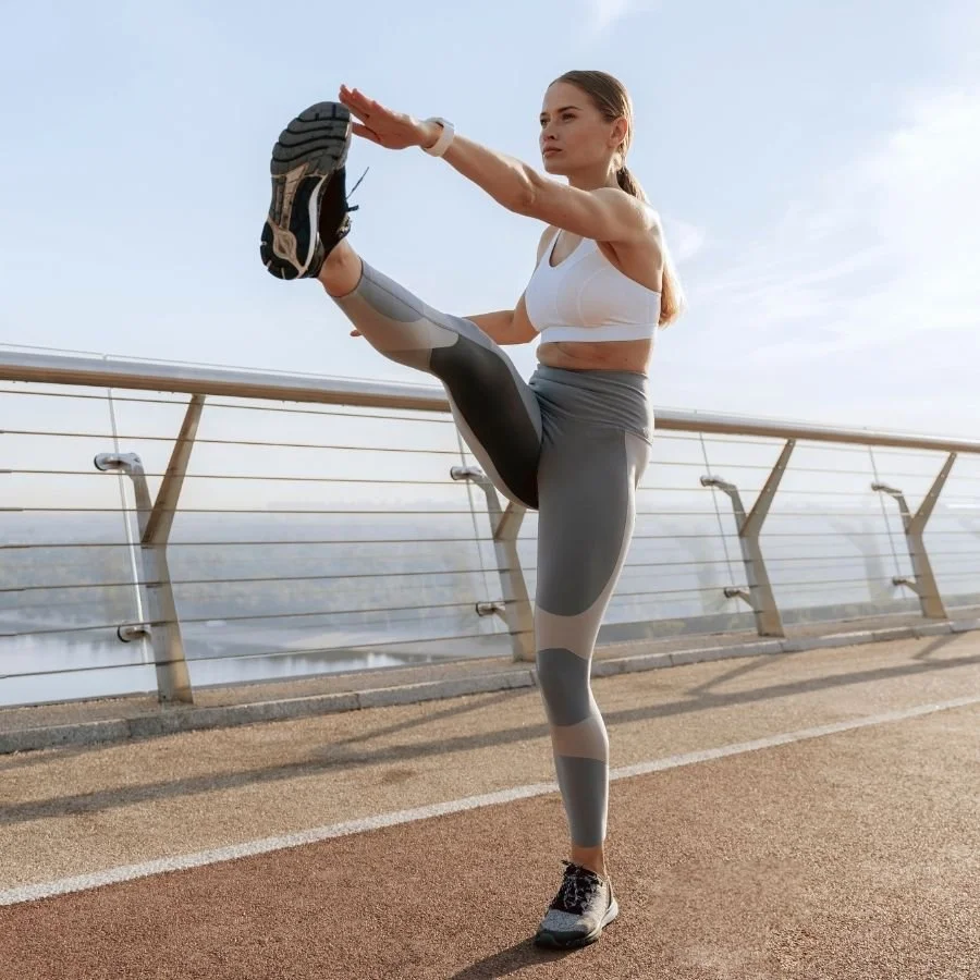 Female athlete performing dynamic leg swings outdoors.