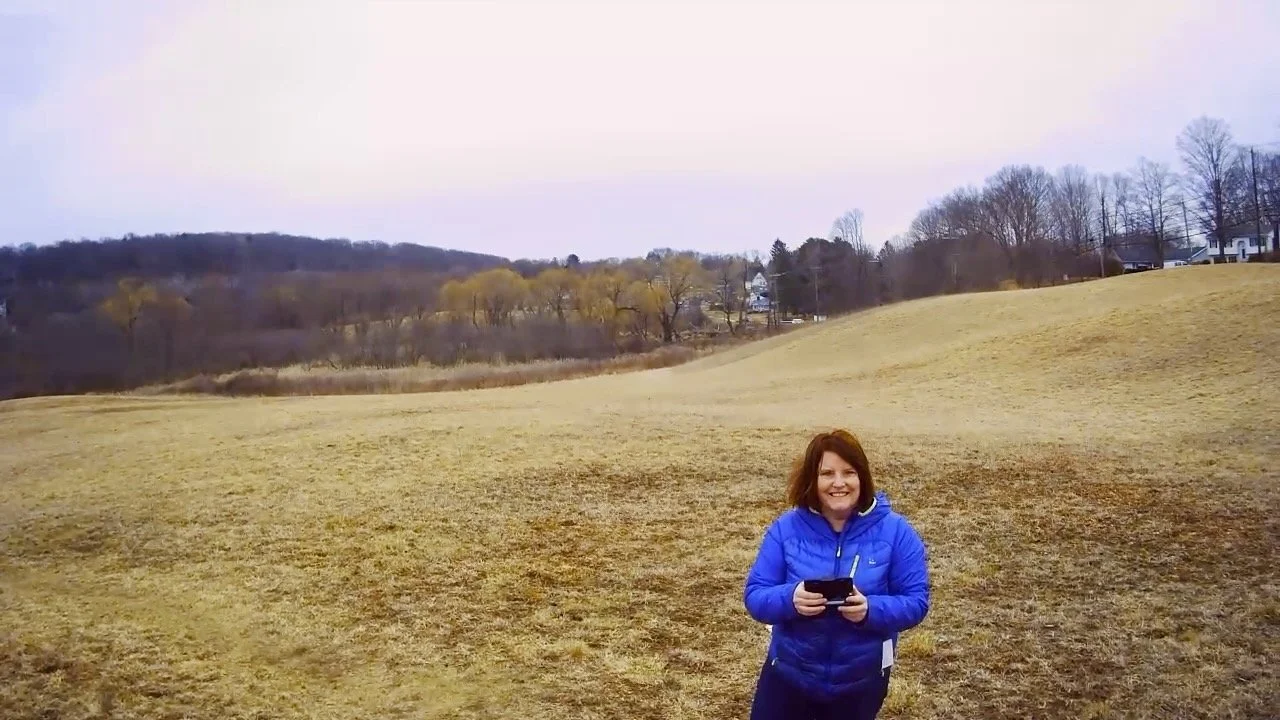 Karin stands in a field taking a selfie with a drone