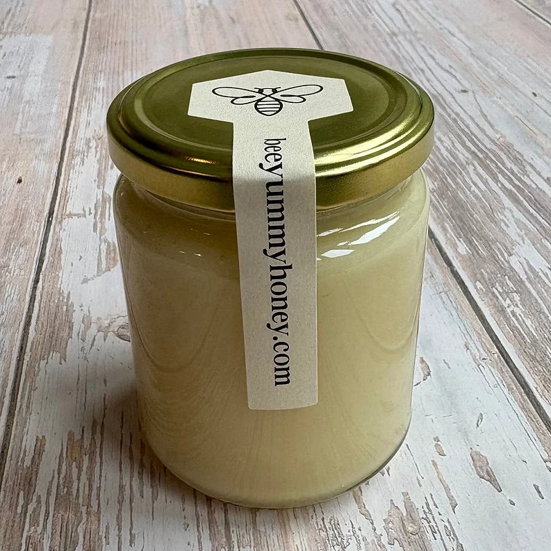 Bee Yummy soft set honey jar with gold lid on a wooden surface.