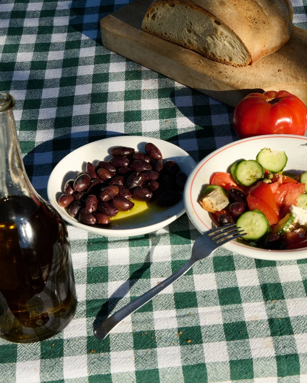 Mediterranean meal with bread, olives, and salad on a checkered tablecloth.
