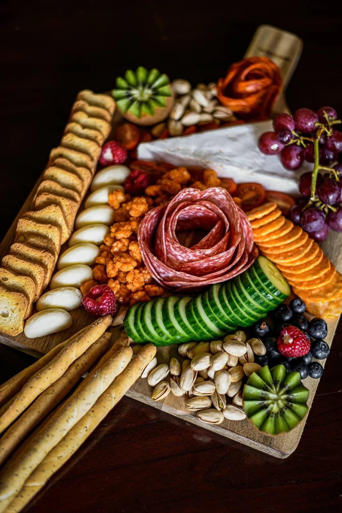 Overhead view of a charcuterie board featuring salami, cheese, crackers, nuts, grapes, cucumber slices and fresh fruit.