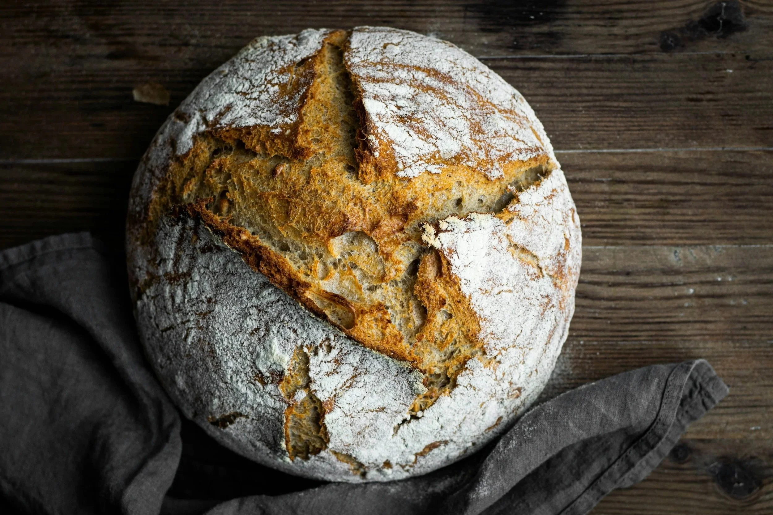 Rustic artisan loaf of bread dusted with flour on a wooden surface.