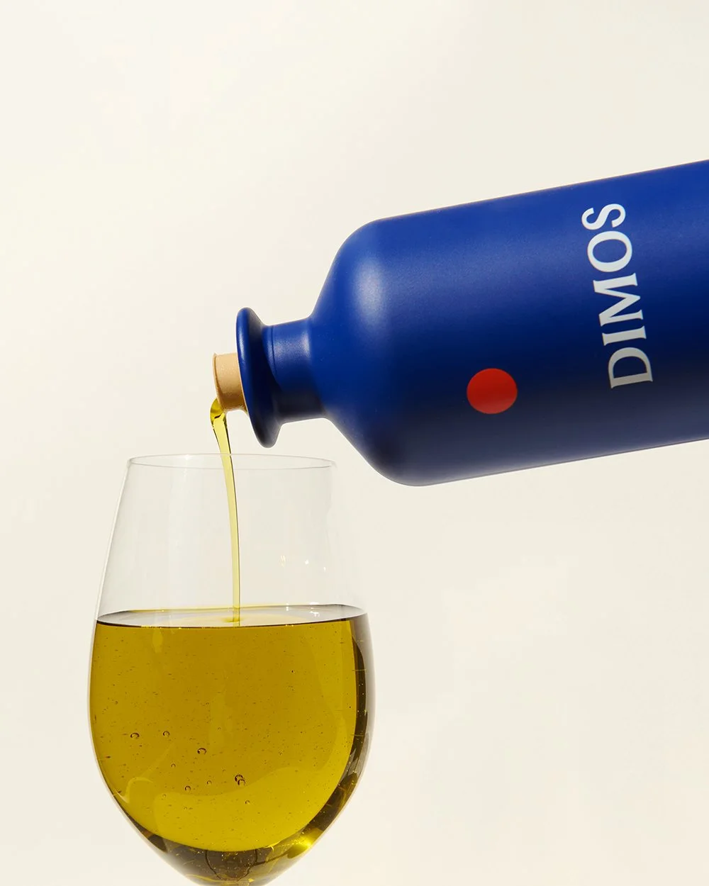 DIMOS olive oil being poured into a glass, showing its golden color and texture.