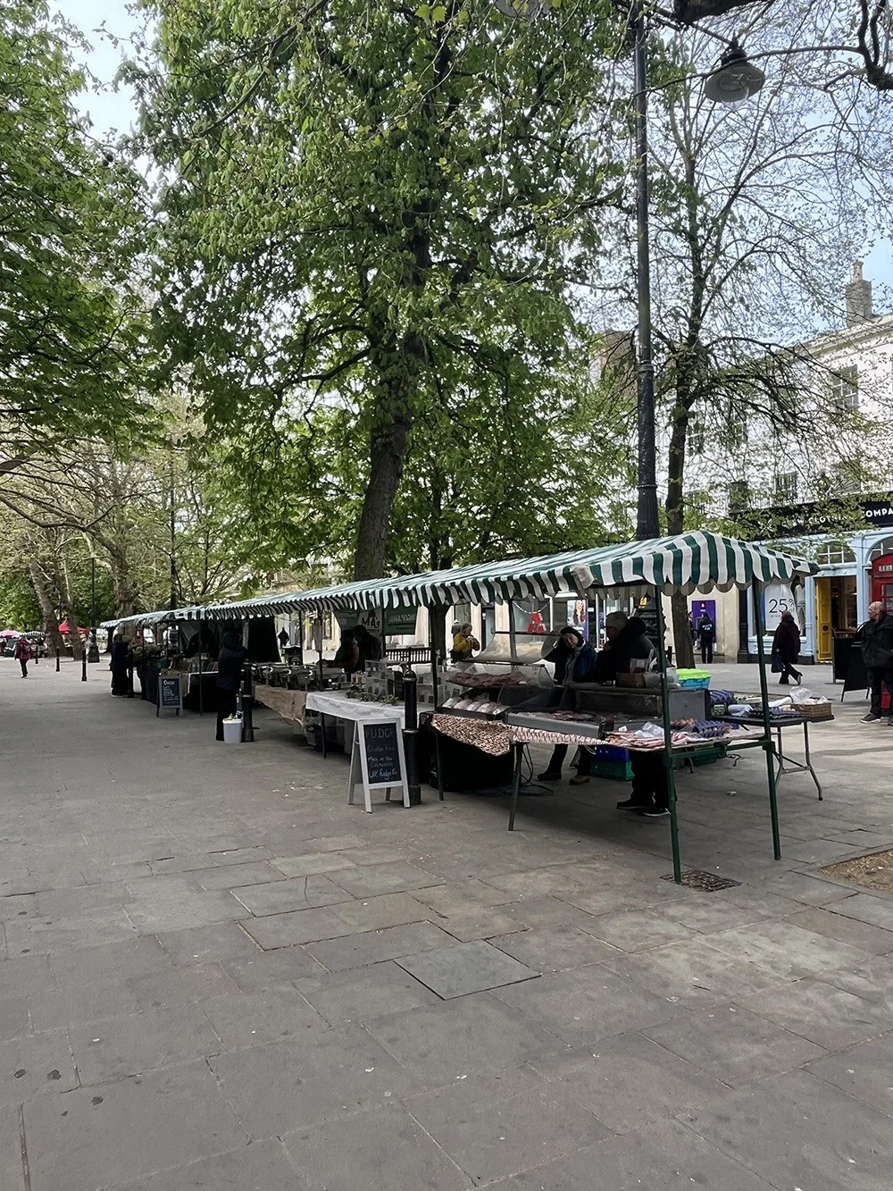 Outdoor market stalls under striped awnings along a tree-lined street.