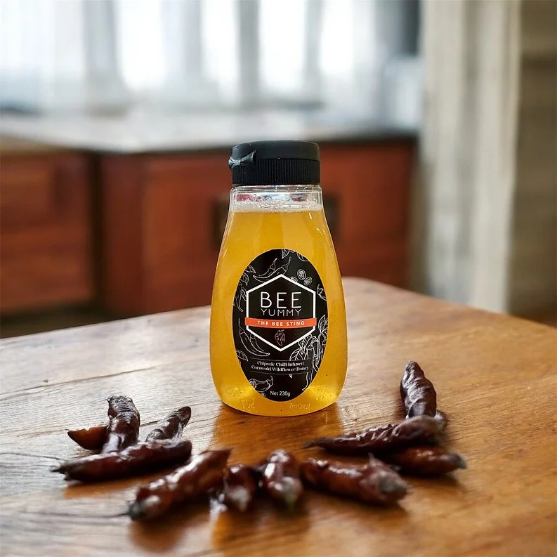 Bee Yummy Bee Sting Hot Honey bottle on a wooden table with dried chillies.