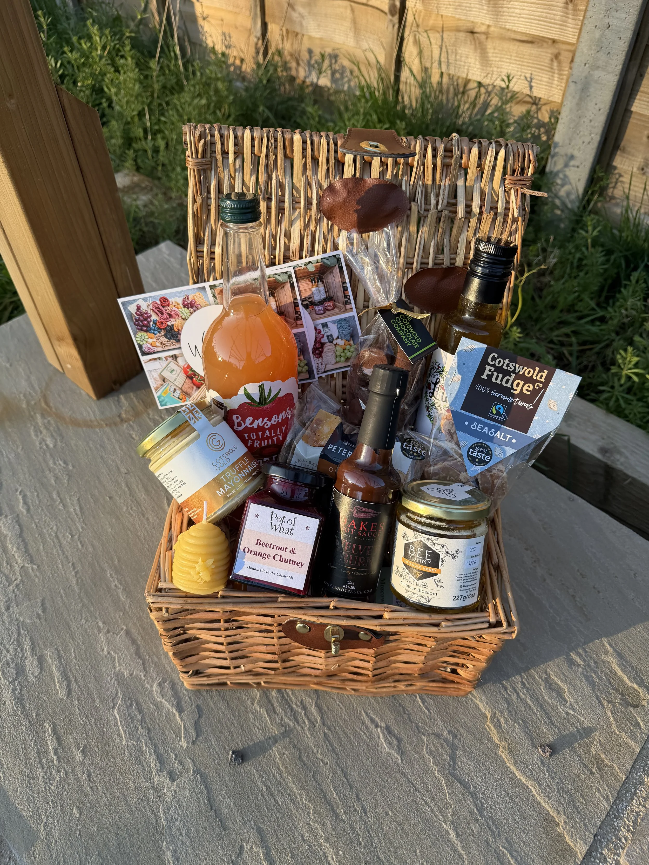 Cotswold hamper with locally made condiments, sweets and drinks in a wicker basket.