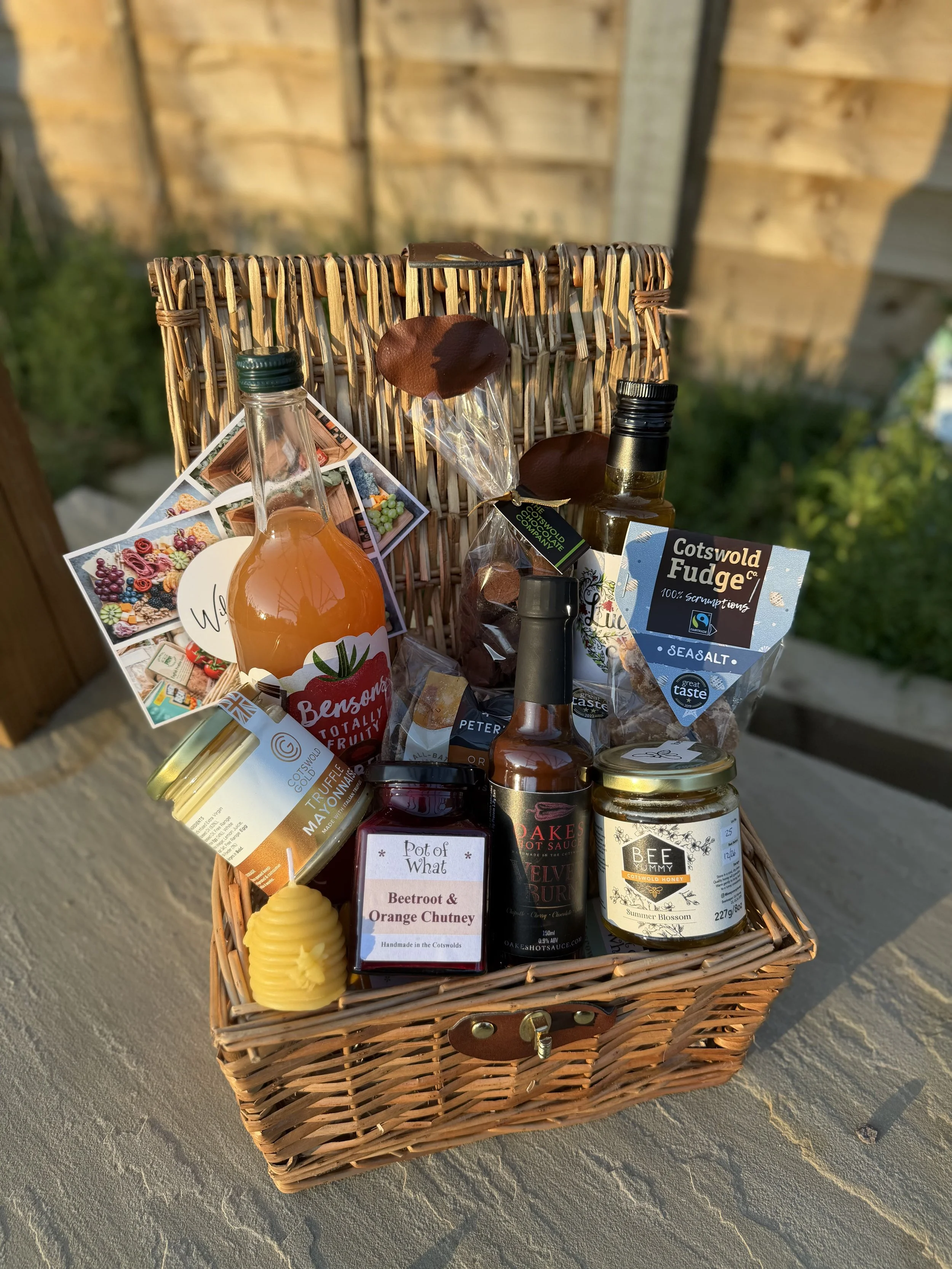 Cotswold food hamper with artisan products in a wicker basket outdoors.
