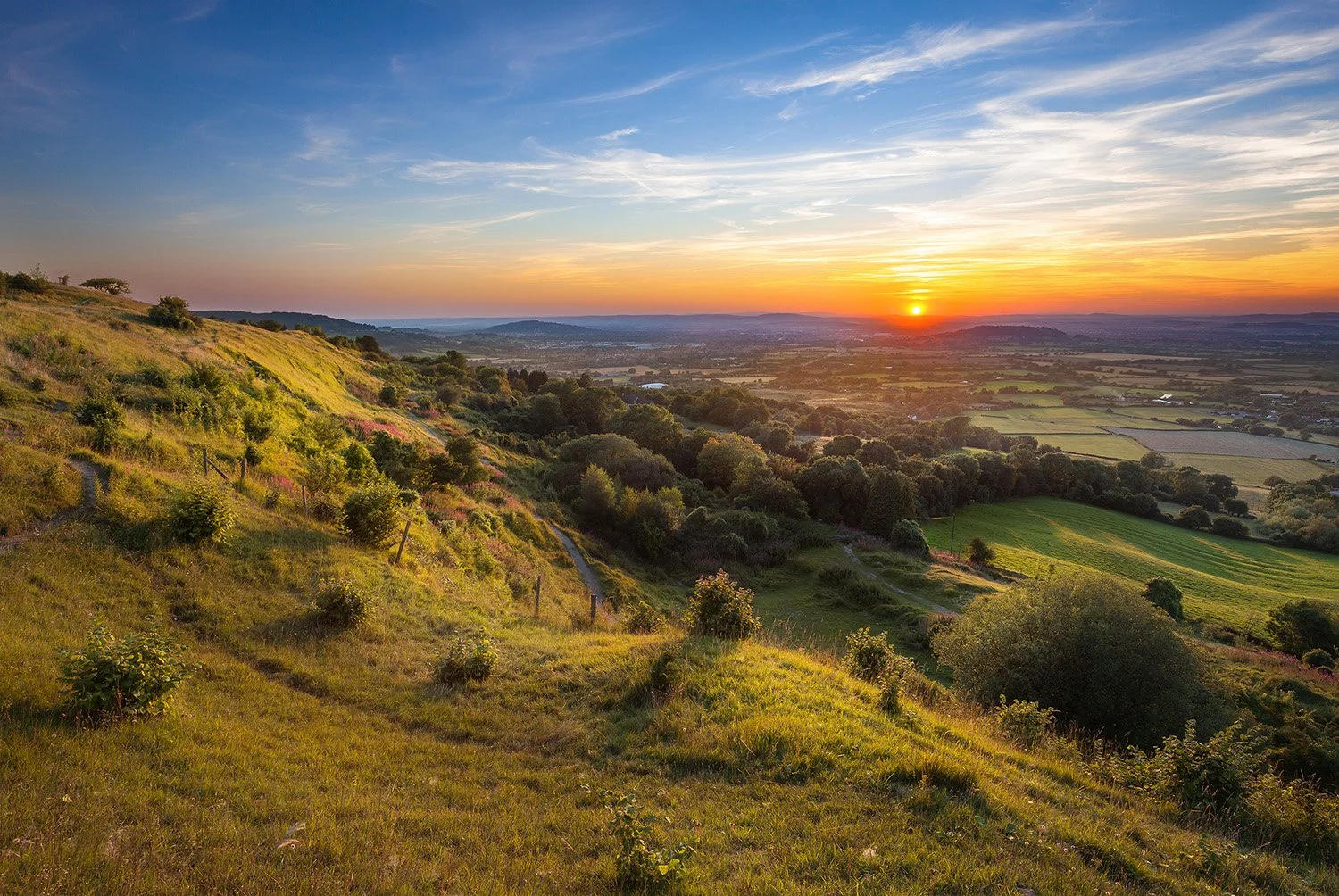 Sunrise over rolling hills and countryside in the Cotswolds.