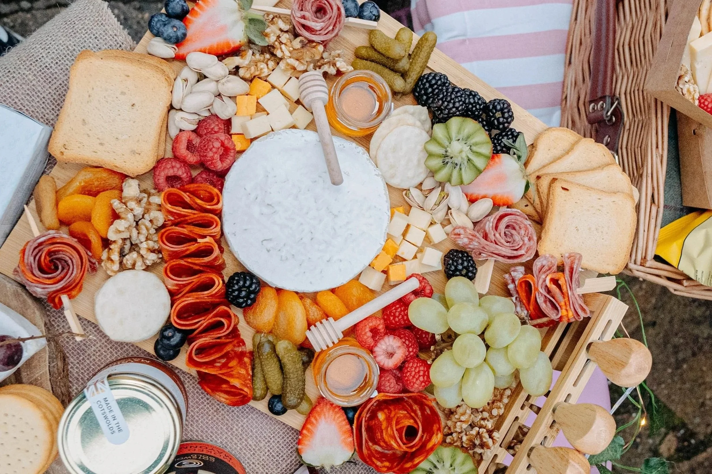 Overhead view of a grazing board with cheeses, charcuterie, fruit, crackers, honey and nuts arranged for sharing.