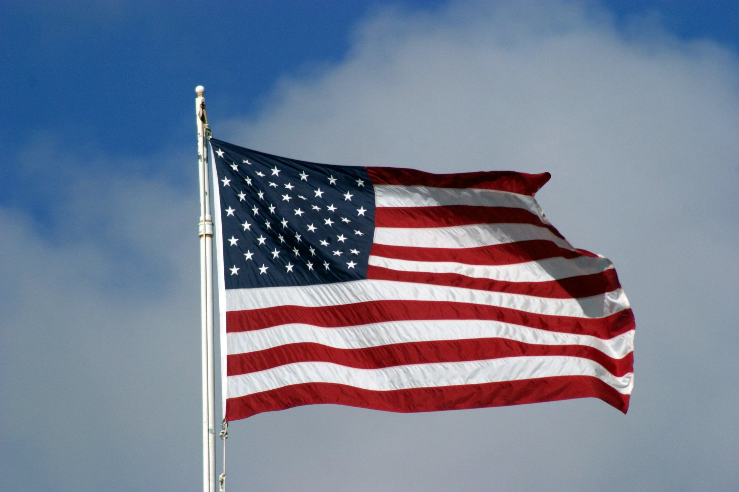 American flag waving against a blue sky with clouds.