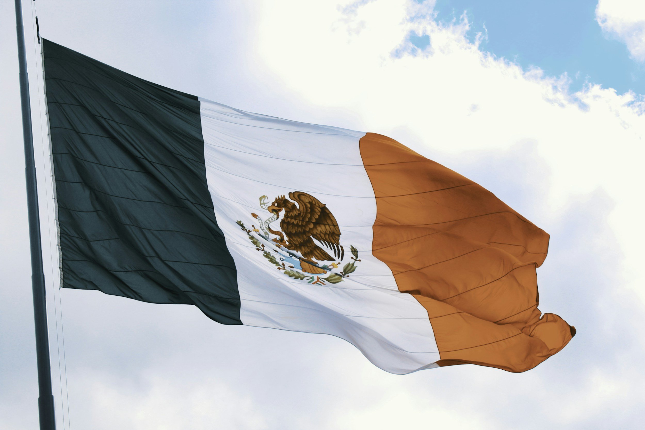 Mexican flag waving against a cloudy sky.