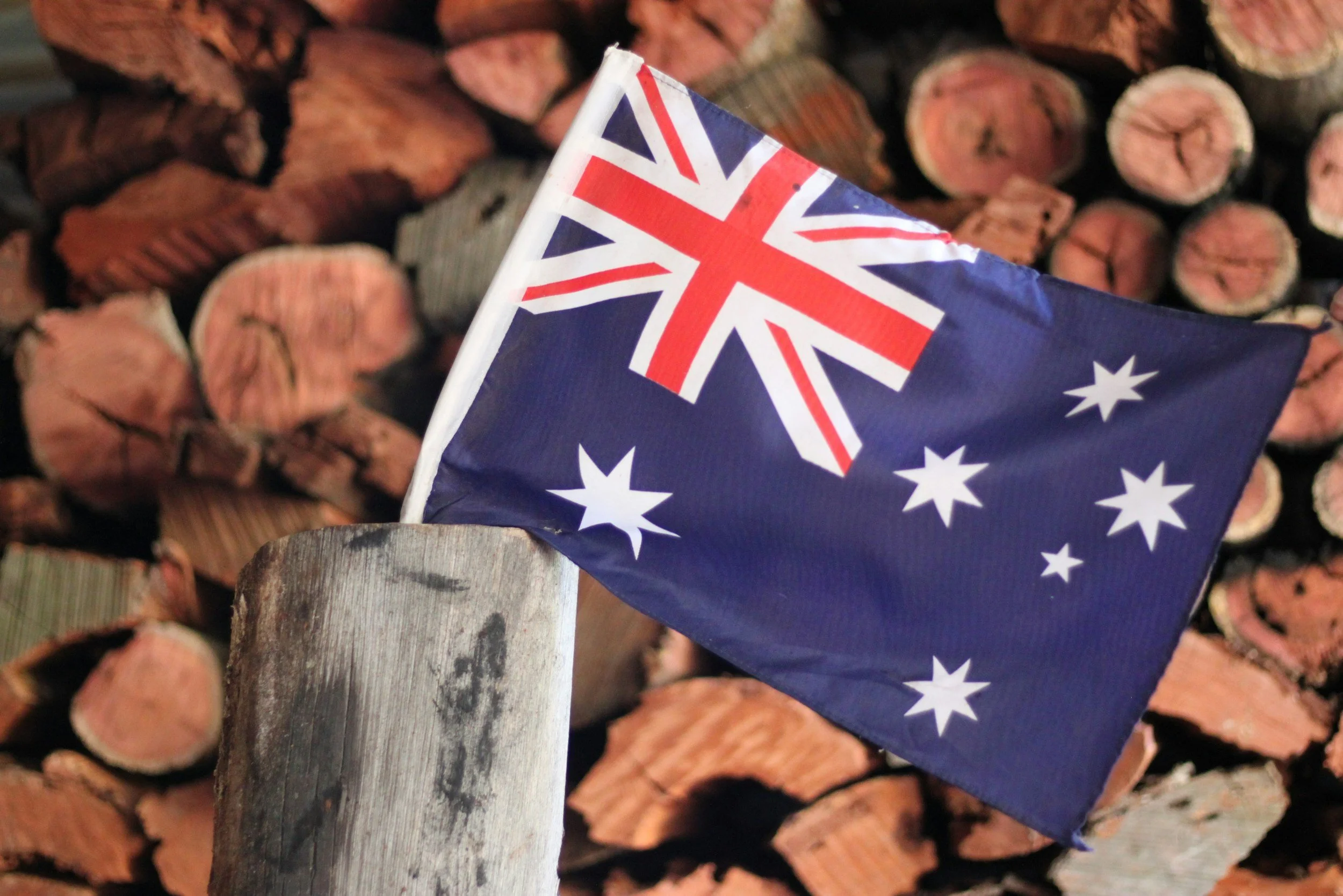 Australian flag on a wooden log with stacked firewood in the background.