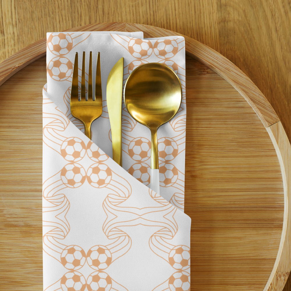 Gold-colored fork, knife, and spoon on a white napkin with a soccer ball pattern on a wooden table.