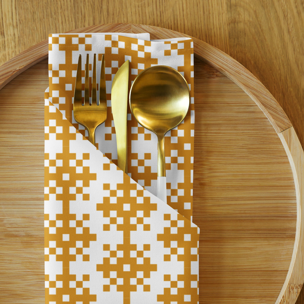Gold-colored fork, knife, and spoon on a patterned paper napkin on a wooden tray.