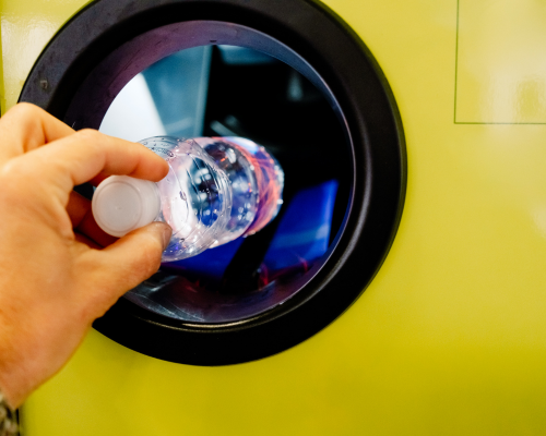 Hand using the return and earn facility to recycle a bottle