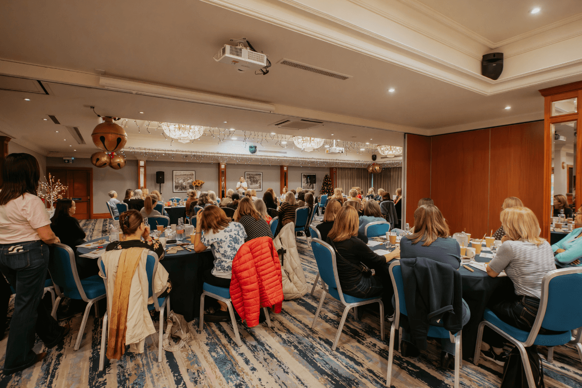 A room filled with widows seated at tables while the retreat leader speaks, creating a safe and supportive Christmas gathering