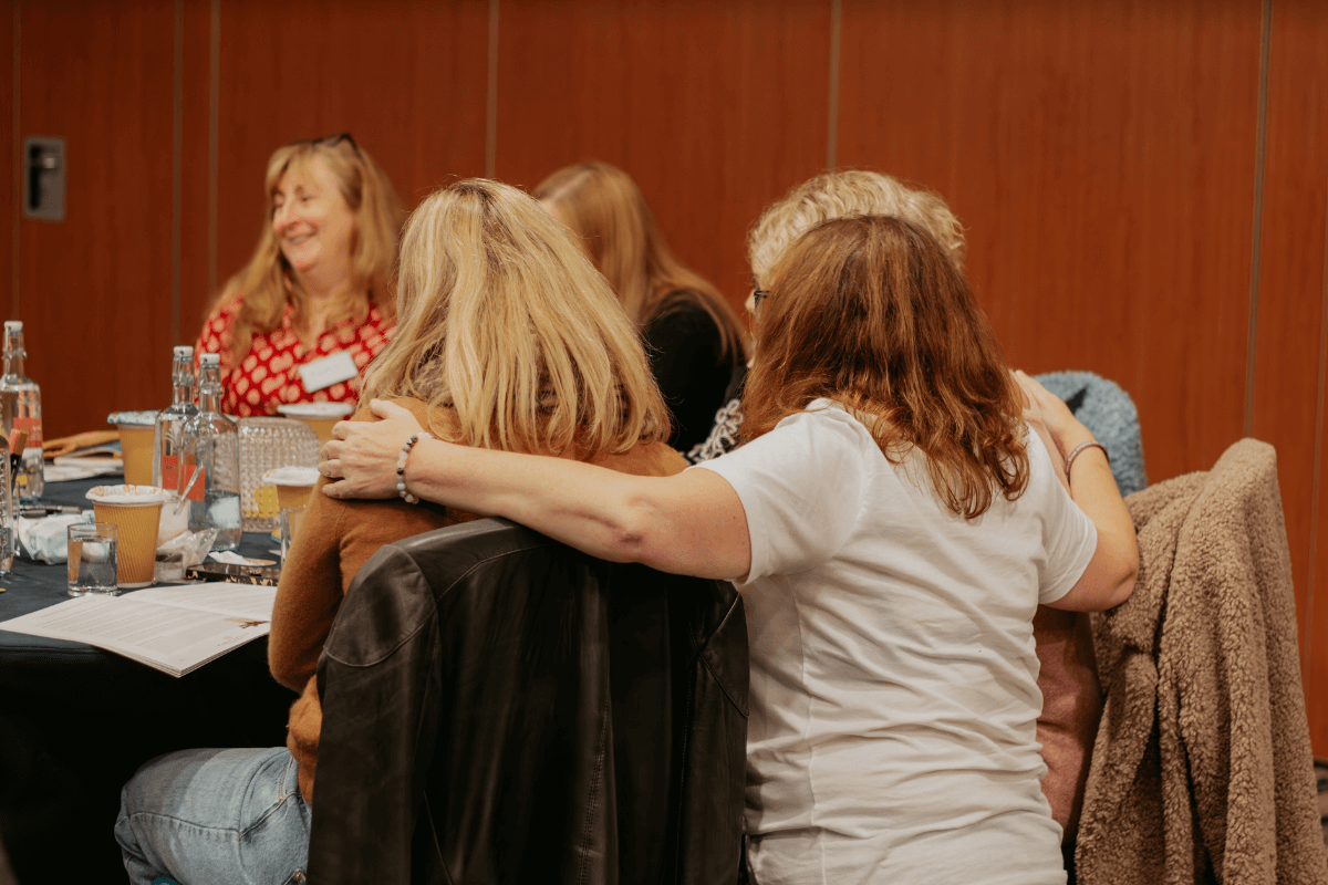 A retreat monitor standing behind two widows with her arms gently around them, offering comfort and emotional support