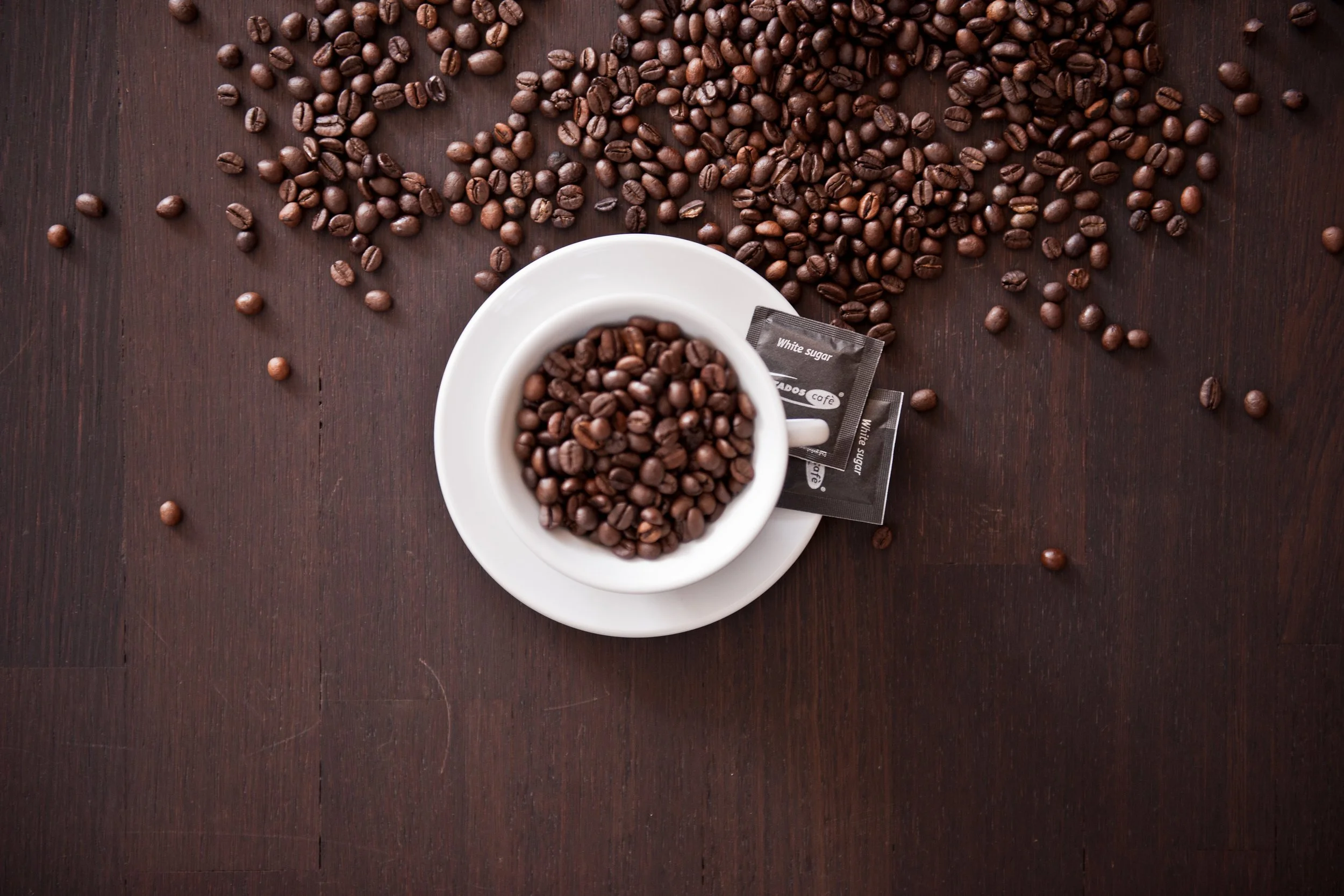 Kaffee Bohnen in weißer Tasse auf einem braunen Holztisch.