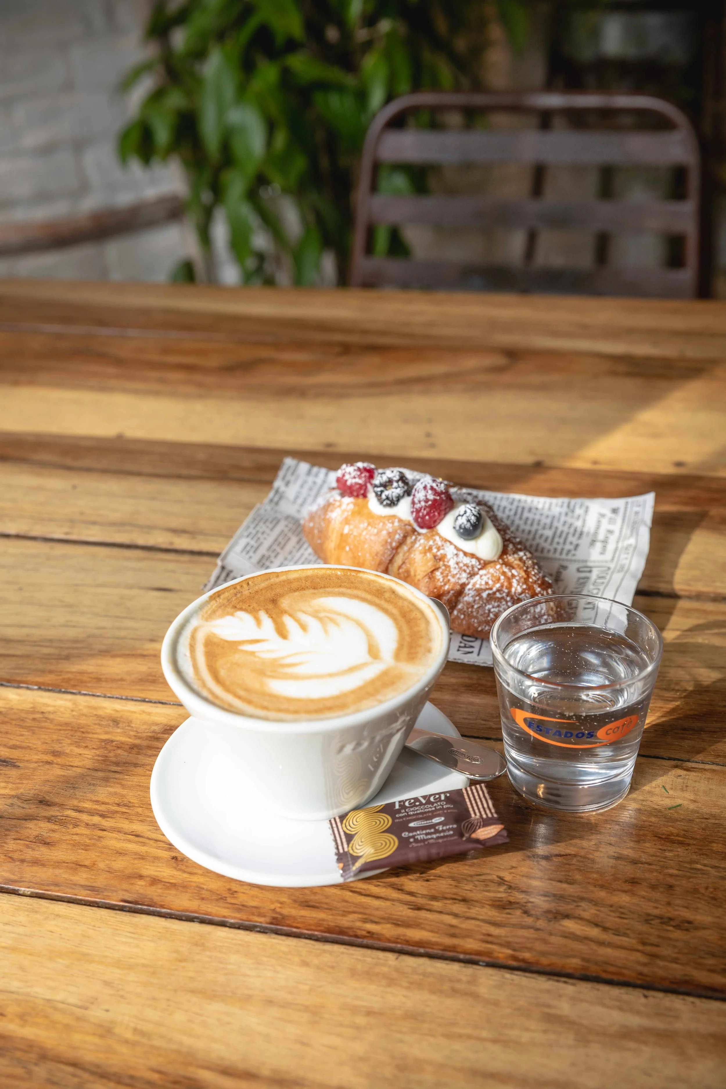 Cappuccino mit Latte Art, Gebäck und Wasser auf Holztisch