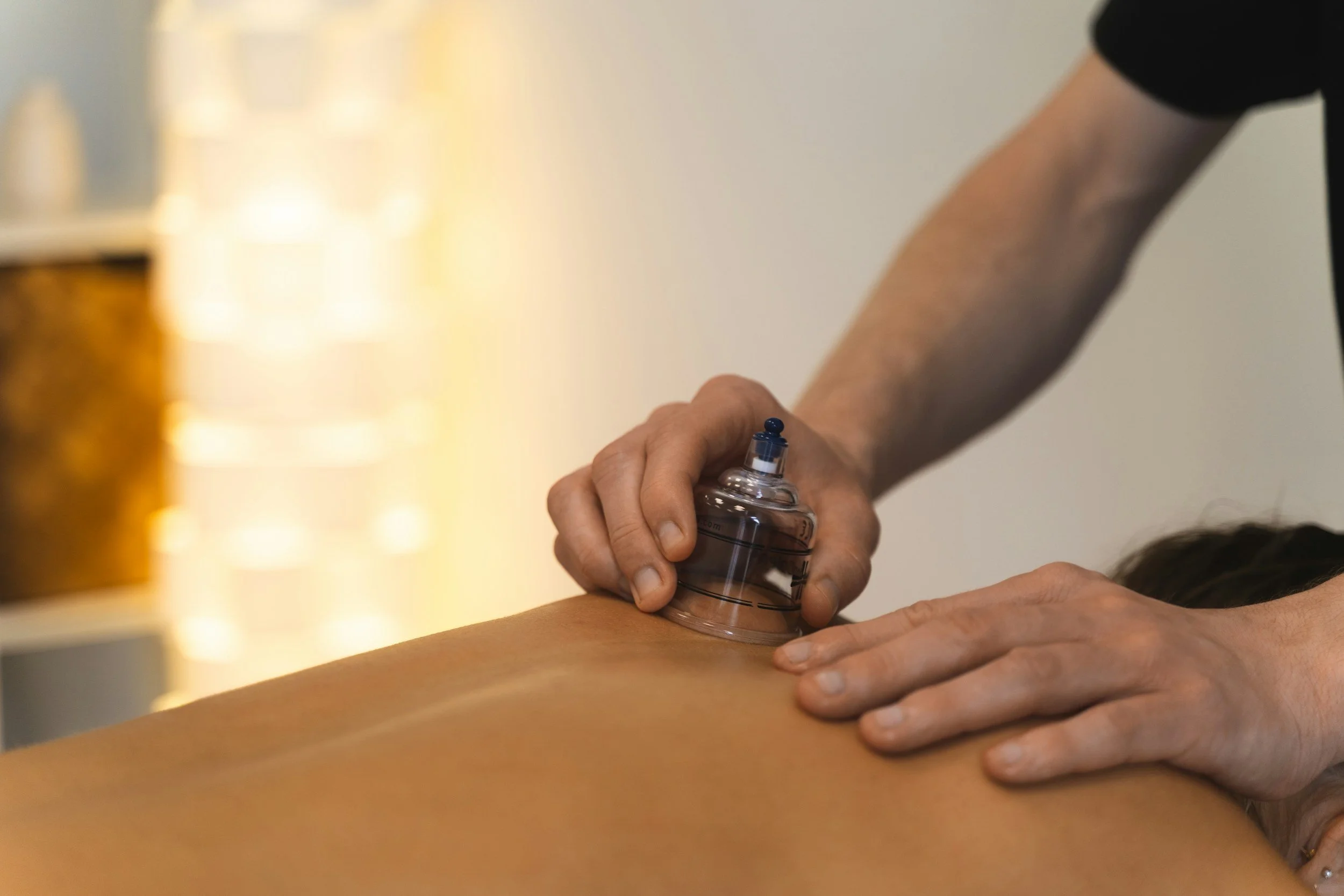 A person receiving a chiropractic or physical therapy adjustment on their lower back from a practitioner who is holding a foam roller.
