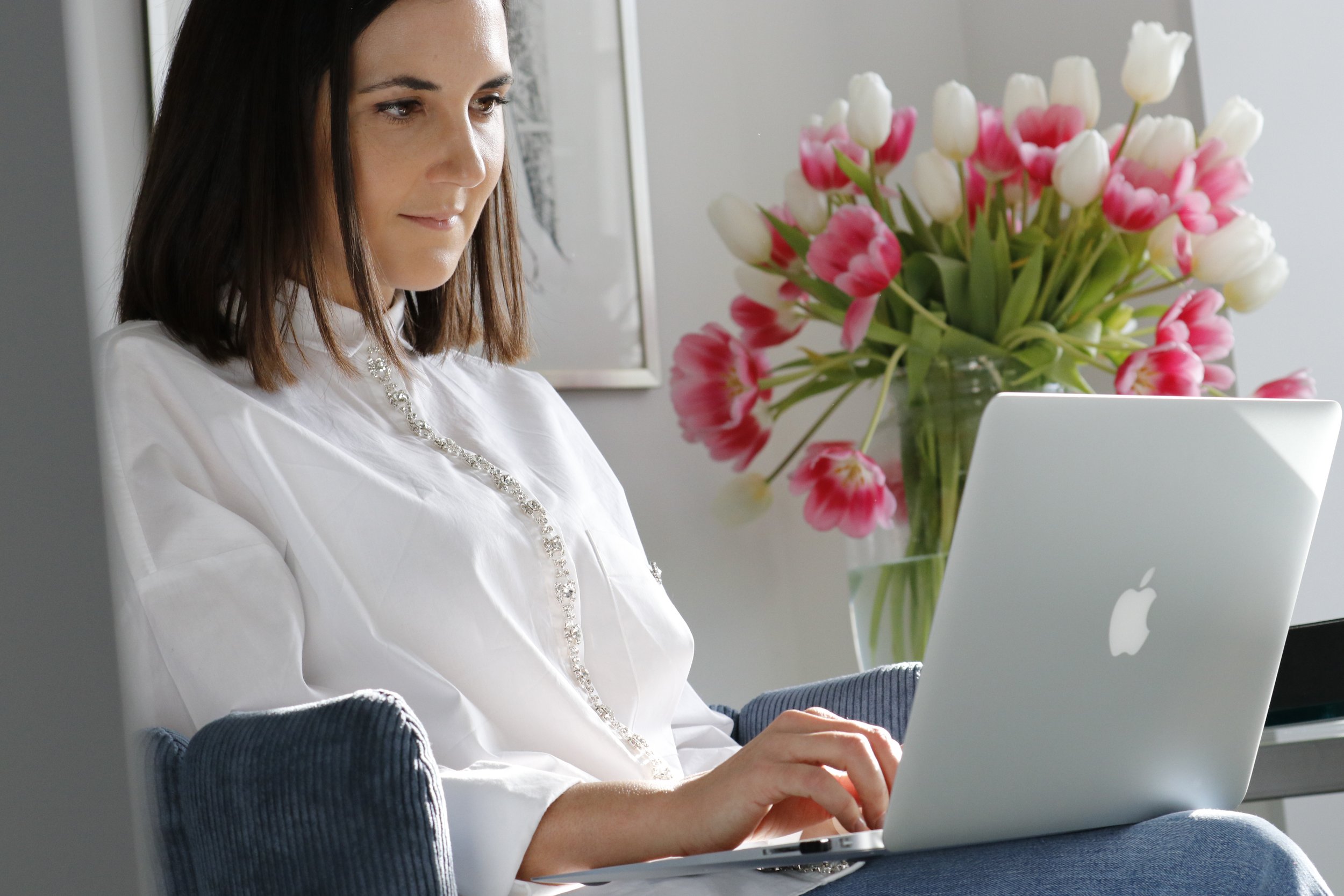 Frau arbeitet an einem MacBook, im Hintergrund eine Vase mit weißen und pinken Tulpen.