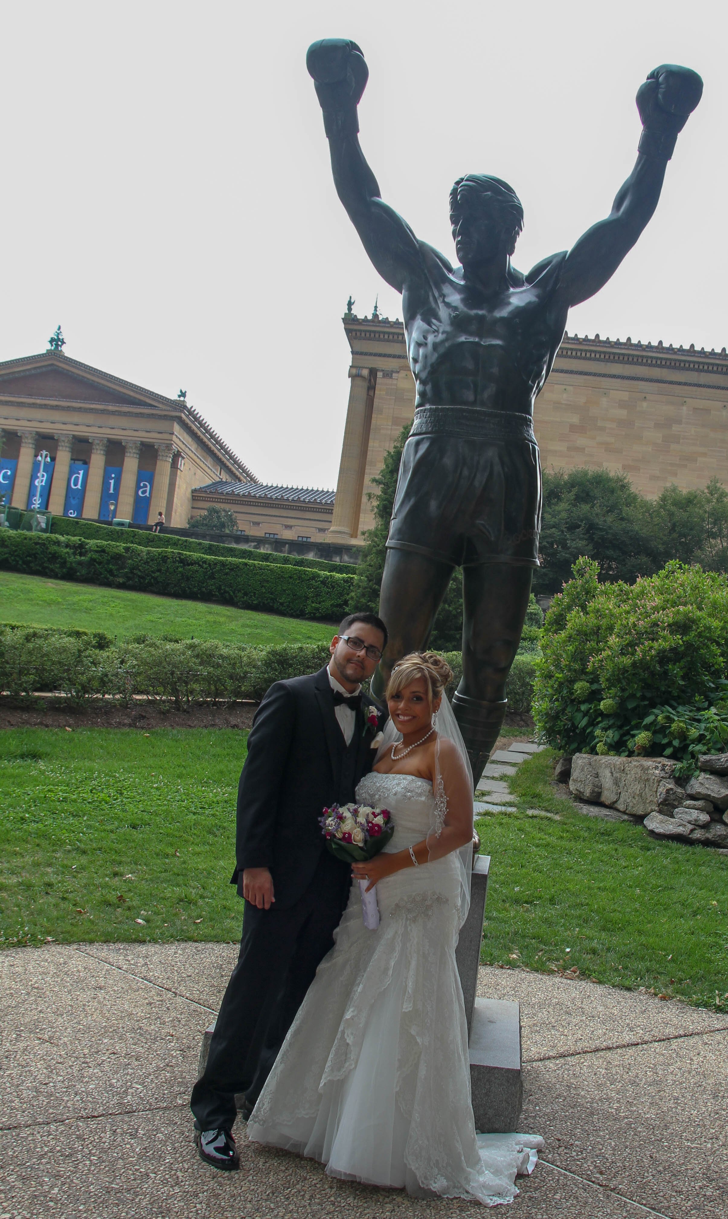 Bride and groom posing by the Rocky Balboa statue in Philadelphia, with the Philadelphia Museum of Art in the background.
