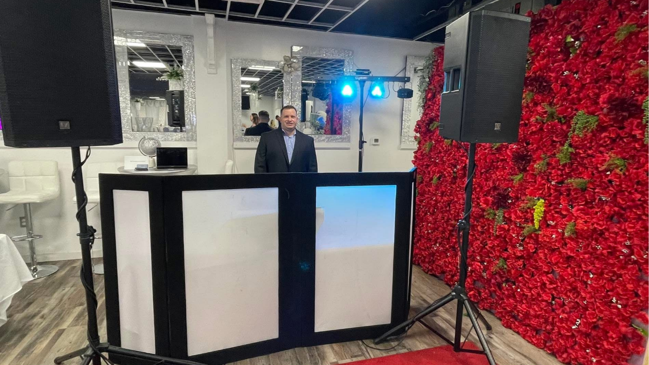 DJ Ian in his booth with speaker system and red rose backdrop.